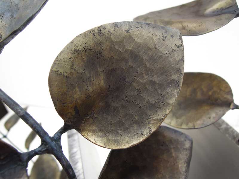 厚みのあるステンレス板の隙間からツルニチニチソウが伸びている様子を鍛鉄で表現したアート作品、葉のアップ。花はワイヤーワーク表現で葉はソリッド表現になっています。丹念なハンマートンと真鍮ブラシで磨きこんだ表情が見て取れます。