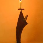 「月のあかり」という鉄の燭台。月の形をした頭部を持つ人のカタチに模したロウソク立てで、灯りを差し出すような佇まいをしています。カタチにより、佑・炬・瑛の３シリーズになっており、祐（ゆう）は、両手を差し伸べて救う、炬（きょ）は、松明のように掲げる火、瑛（えい）は、光り輝く玉という意味があります。暗い中で小さな和蝋燭を灯した状態での写真です。頭部の影が月のカタチに揺れて、個体によってはスリットから漏れる光が日輪となったり、または三日月となったりします。