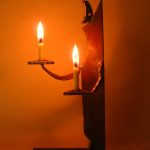 「月のあかり」という鉄の燭台。月の形をした頭部を持つ人のカタチに模したロウソク立てで、灯りを差し出すような佇まいをしています。カタチにより、佑・炬・瑛の３シリーズになっており、祐（ゆう）は、両手を差し伸べて救う、炬（きょ）は、松明のように掲げる火、瑛（えい）は、光り輝く玉という意味があります。暗い中で小さな和蝋燭を灯した状態での写真です。頭部の影が月のカタチに揺れて、個体によってはスリットから漏れる光が日輪となったり、または三日月となったりします。