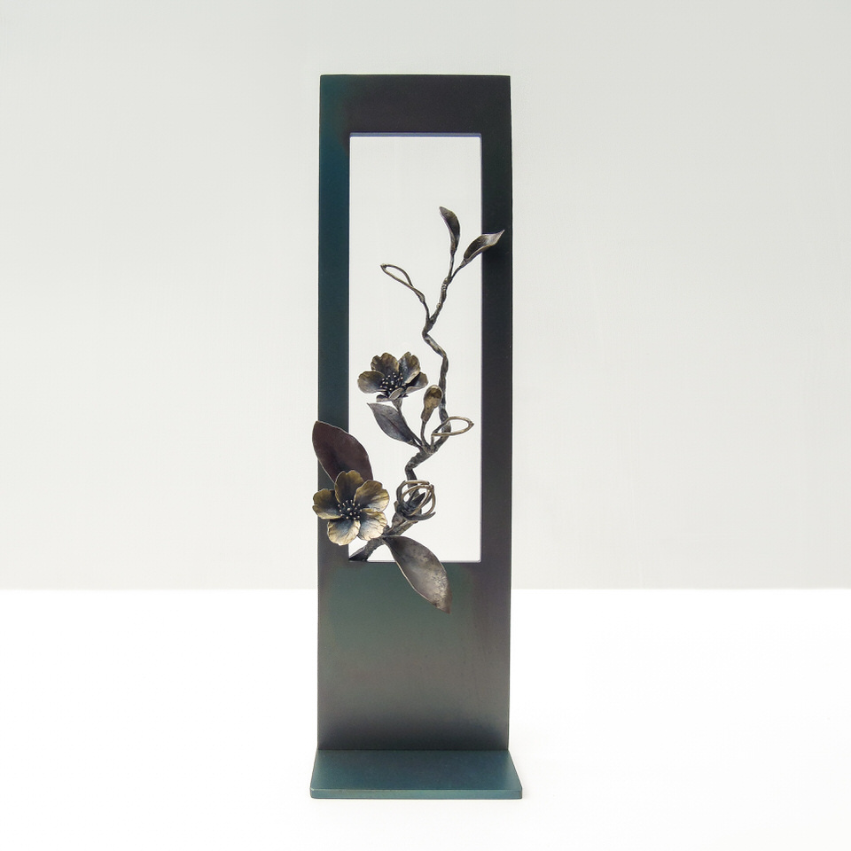 縦長のプレートに開いた窓からひと枝の山桜がのぞいている様子を鉄で表現したアート作品です。実際の桜の花と同じ大きさです。