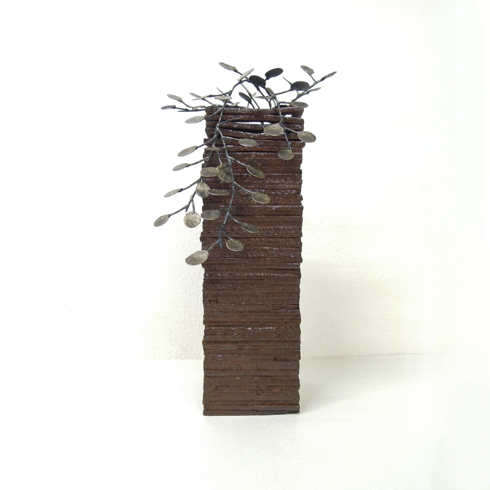積層した鉄板の上部からワイヤープランツがこぼれている鍛鉄のアート作品です。手切りした鉄板の断面の繋がりと細かくハンマートーンの入った小さな葉の数々がリズムを作っています。