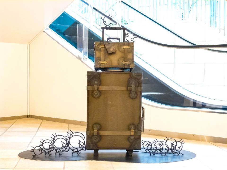 横浜ノースポートモールにオープン時設置されていたアートオブジェ「急ぐヤツら」。忘れ物のバッグや鞄を届けるために駅へと急いでいる彫刻作品です。全て鉄で制作されました。旅行カバンを運ぶ作品。