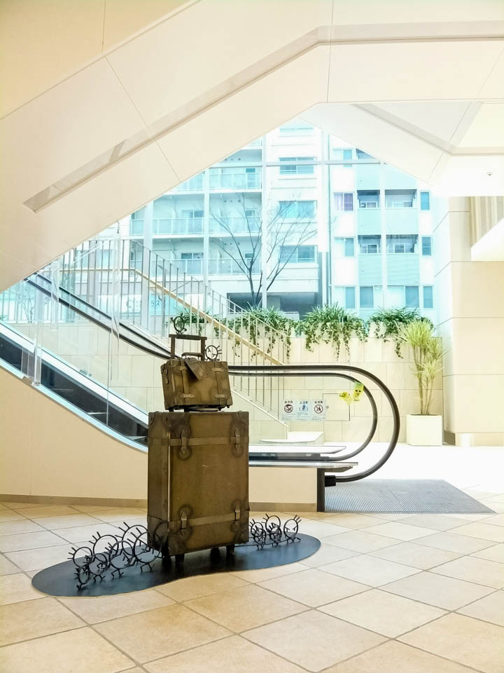 横浜ノースポートモールにオープン時設置されていたアートオブジェ「急ぐヤツら」。忘れ物のバッグや鞄を届けるために駅へと急いでいる彫刻作品です。全て鉄で制作されました。旅行カバンを運ぶ作品。