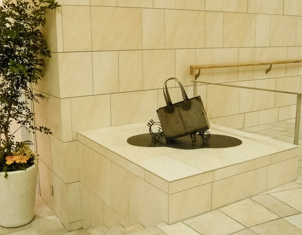 横浜ノースポートモールにオープン時設置されていたアートオブジェ「急ぐヤツら」。忘れ物のバッグや鞄を届けるために駅へと急いでいる彫刻作品です。全て鉄で制作されました。トートバッグを運ぶ作品。