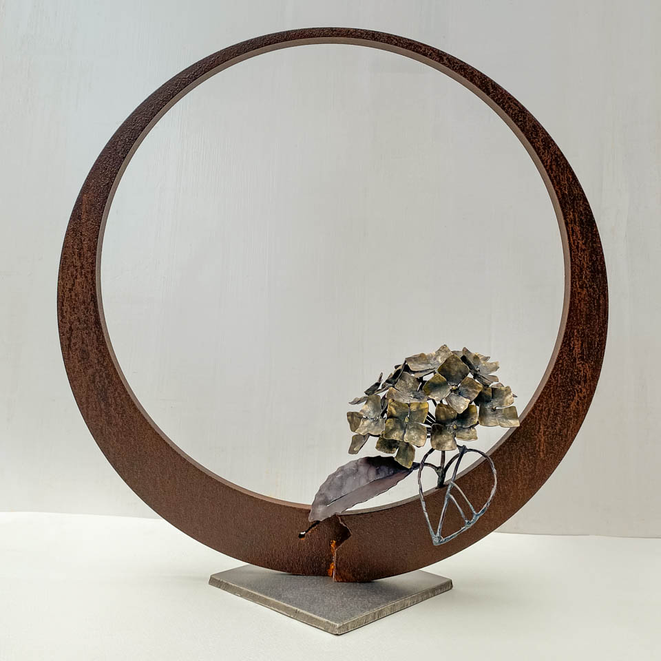紫陽花のこんもりした花が円の中に添えられているアート作品、鉄の彫刻です。柔らかい花びらを模した鉄のアジサイの花に、面と線で表現した葉が寄り添っています。