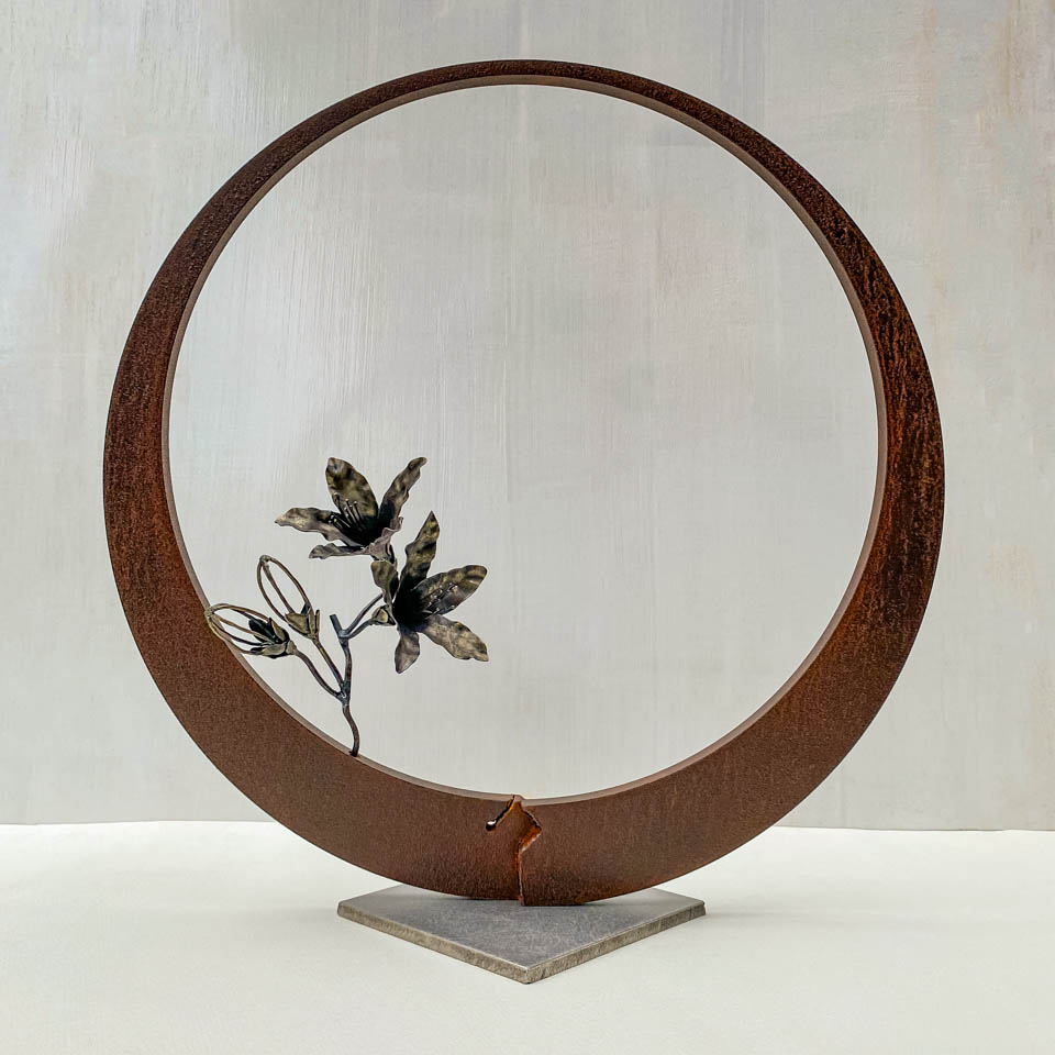 箱根の春を彩るミツバツツジの花を円弧に添えた鉄の彫刻、アート作品です。スタンドタイプです。蕾は鍛造した鉄線で表現し軽い印象になっています。円弧は厚みのある鉄を切り出し、下部でズラして表情をつけています。