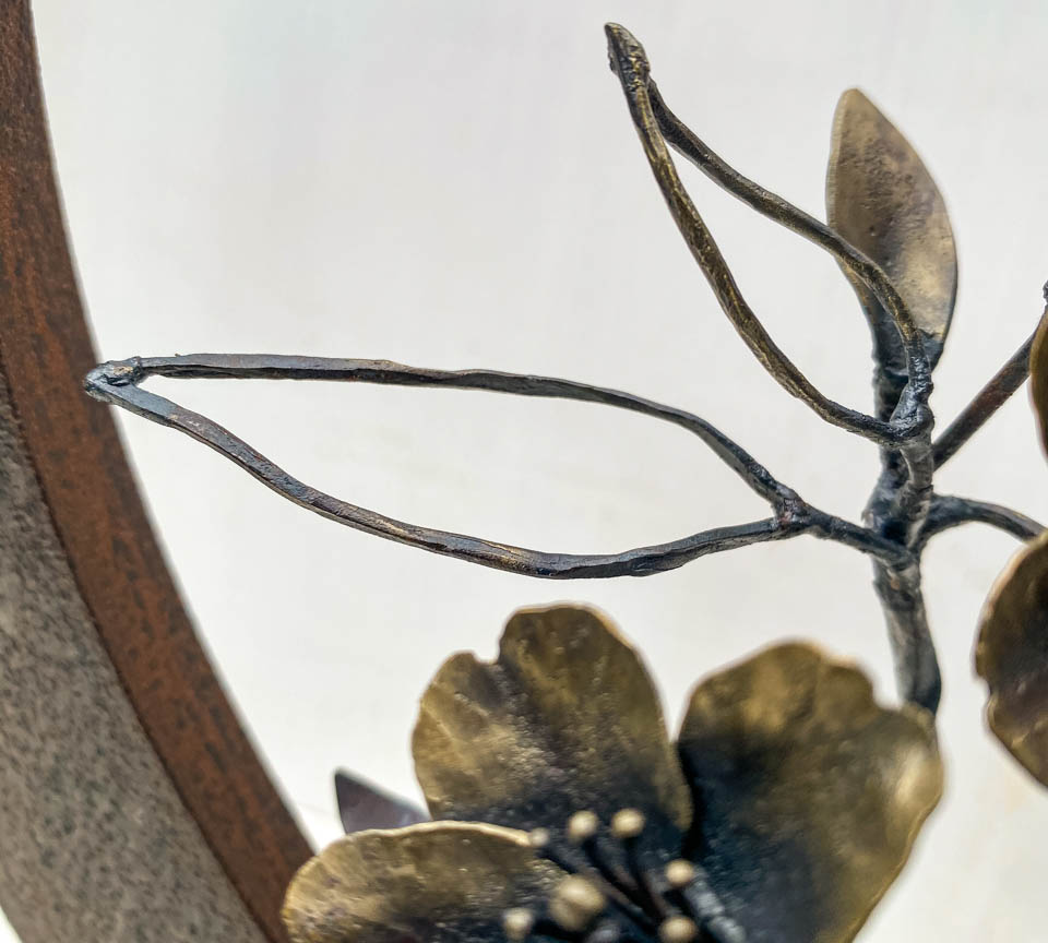 箱根に咲くマメザクラの小さな枝が、丸いベースに添えられた鉄の彫刻です。かわいい花が鉄で繊細に表現され、新芽が芽吹いています。線の葉の表現。