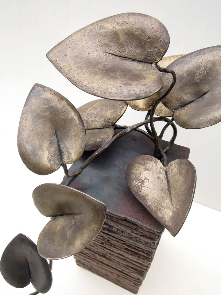 蔓(カズラ)をモチーフにした鉄の彫刻、アートオブジェです。 ツルが上から下へ垂れながら葉を光に向かって持ち上げる様子を、躍動感ある姿として表現しました。 一枚はアクセントとして黒みのある仕上がりとし、他は真鍮ブラシで磨き込み黄色みを帯びた控えめが光沢があります。 厚みのある鉄板を重ねたベースからツルがこぼれ出ている姿です。 葉の表情。