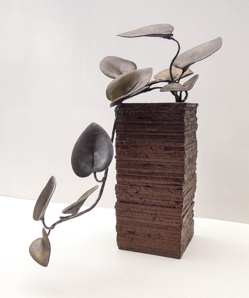 蔓(カズラ)をモチーフにした鉄の彫刻、アートオブジェです。 ツルが上から下へ垂れながら葉を光に向かって持ち上げる様子を、躍動感ある姿として表現しました。 一枚はアクセントとして黒みのある仕上がりとし、他は真鍮ブラシで磨き込み黄色みを帯びた控えめが光沢があります。 厚みのある鉄板を重ねたベースからツルがこぼれ出ている姿です。