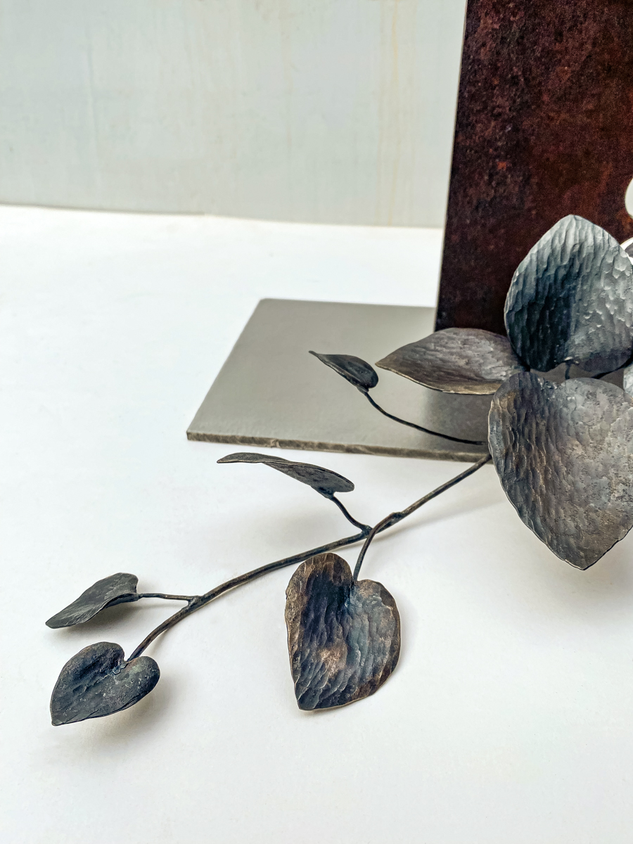 丸い開口が連なる表情豊かな鉄の厚板に、カンガルーアイビーのツルが肩から下がるよう配置した鉄のアート作品です。華やかな大小の葉がリズミカルに連なり、軽やかな印象の彫刻作品になっています。ツルの先端の表情。