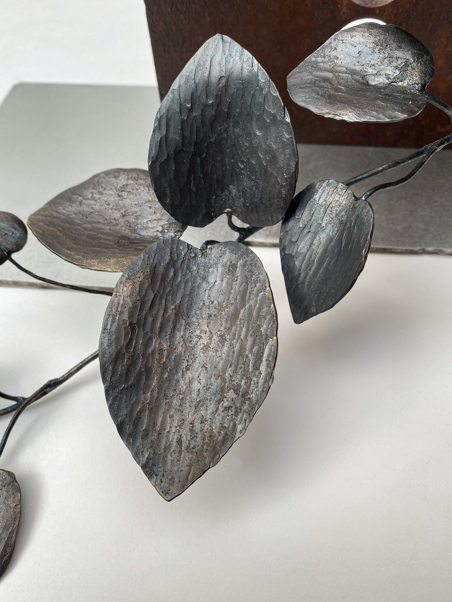 丸い開口が連なる表情豊かな鉄の厚板に、カンガルーアイビーのツルが肩から下がるよう配置した鉄のアート作品です。華やかな大小の葉がリズミカルに連なり、軽やかな印象の彫刻作品になっています。葉の表情。