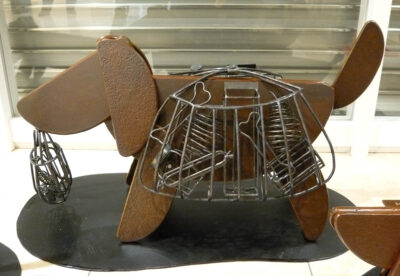 笑顔の口元の形でもある、半円形を集めて作った犬のアート彫刻。買い物袋を背負っています。