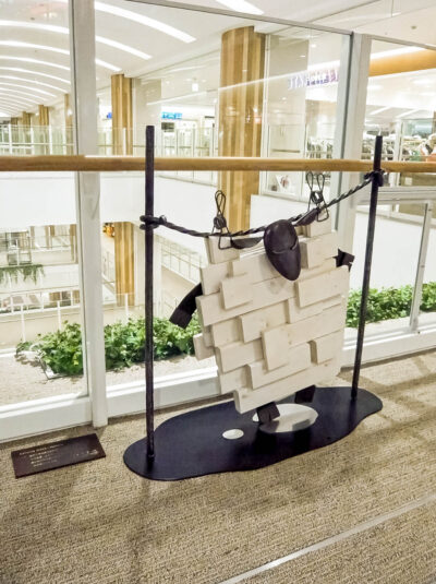 木と鉄で創られた羊のオブジェ彫刻。洗濯された羊が吊るされて干されている様子。足元には水たまりができています。